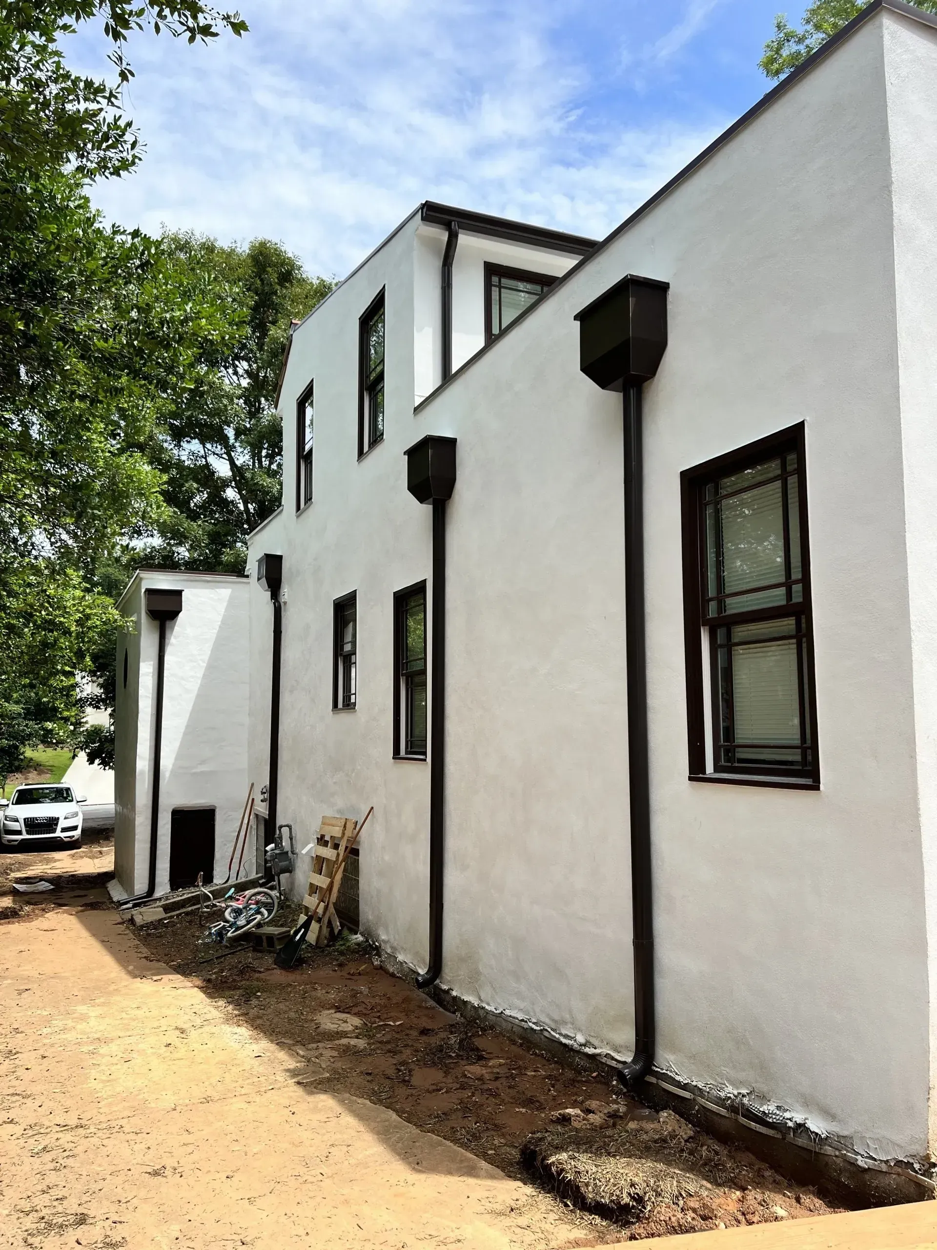 White building with dark gutters and windows. Exterior shot with unfinished landscaping and a vehicle.