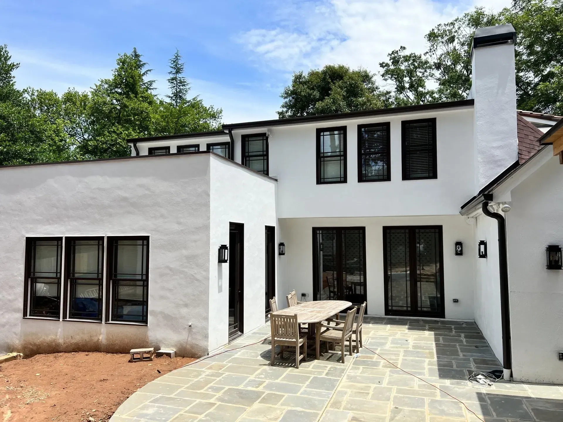 Exterior view of a white stucco house with black framed windows, a patio, and a table with chairs.
