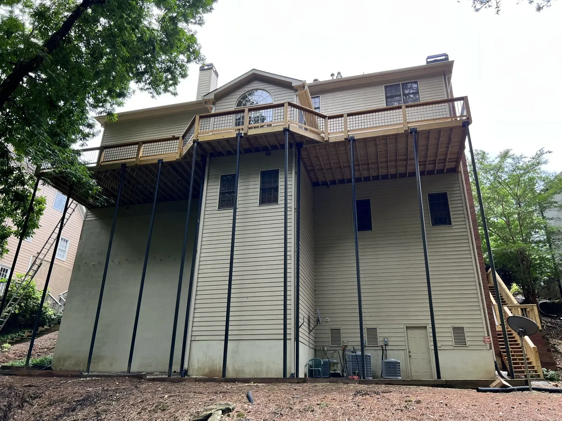 Back of a two-story beige house with a large wooden deck supported by black metal poles.