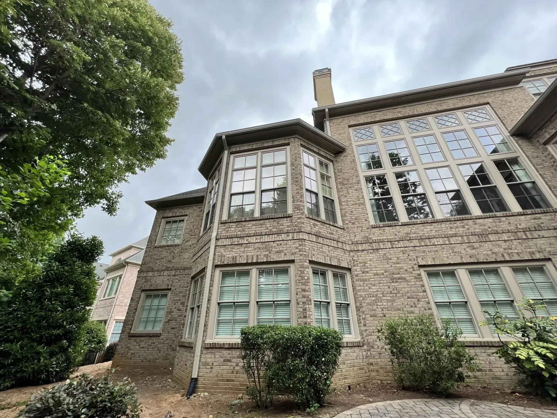 Stone facade of a multi-story house with numerous windows, under a cloudy sky.
