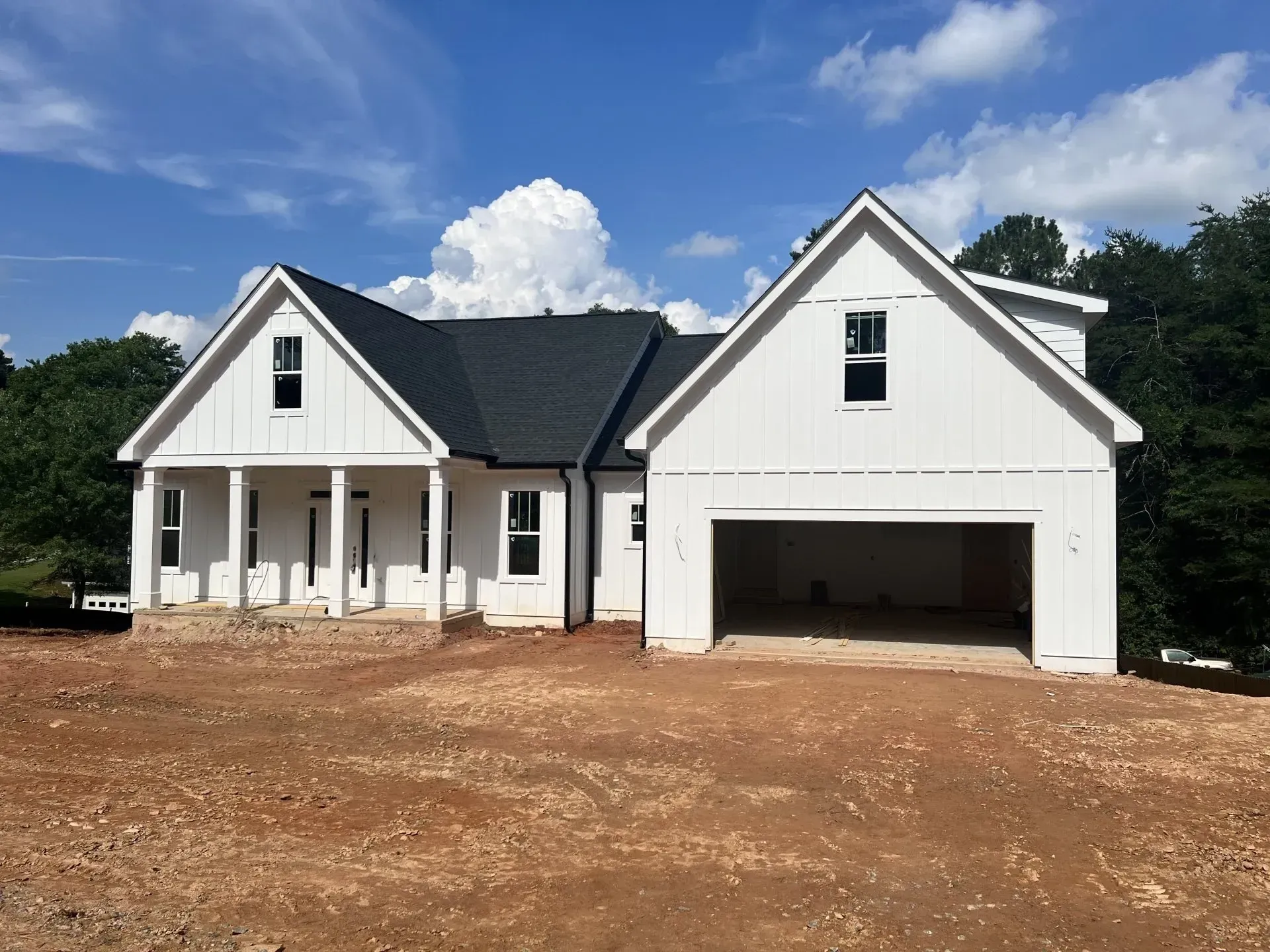 White house under construction, with open garage, on a dirt lot, against a blue sky.
