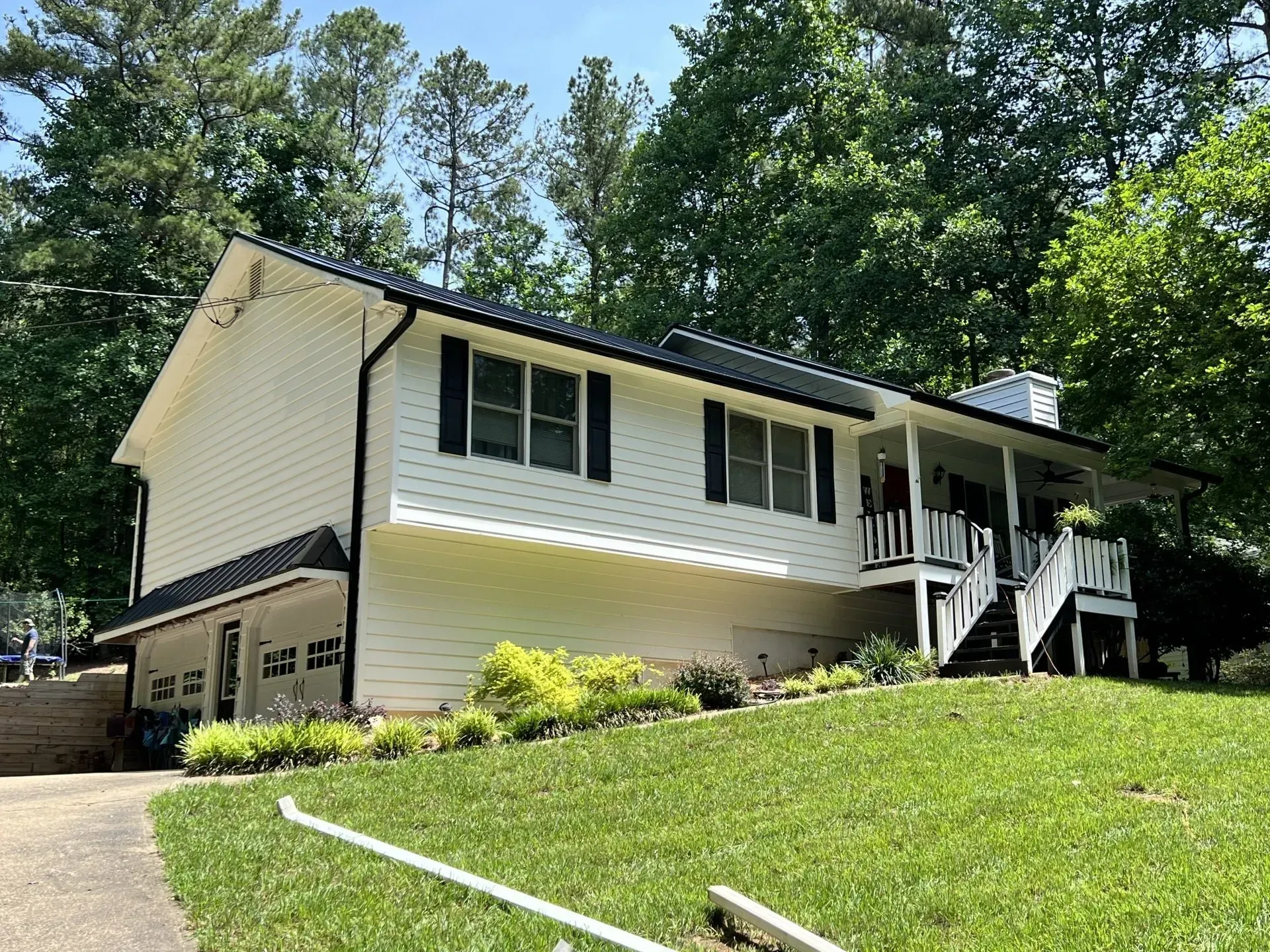White house with black shutters, roof, and trim on a grassy hill; trees in the background.