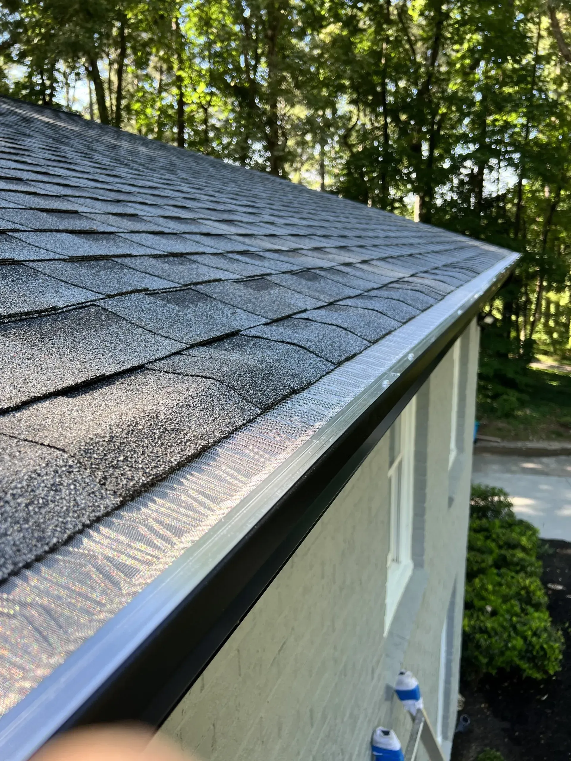 Close-up view of a house roof with dark gray shingles, white gutters, and a light-colored brick exterior.