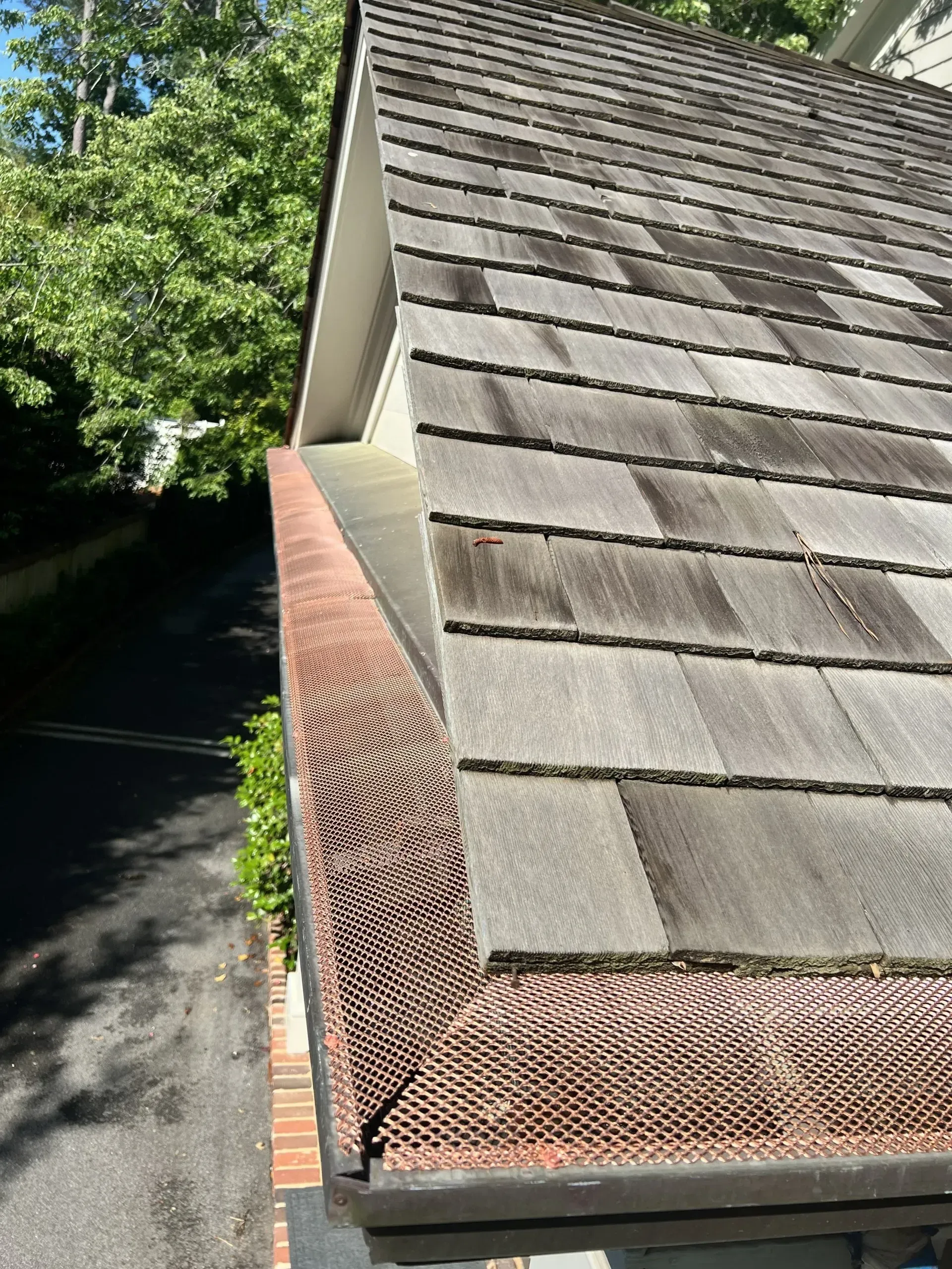 Copper-colored gutter guards installed along the edge of a cedar shake roof.