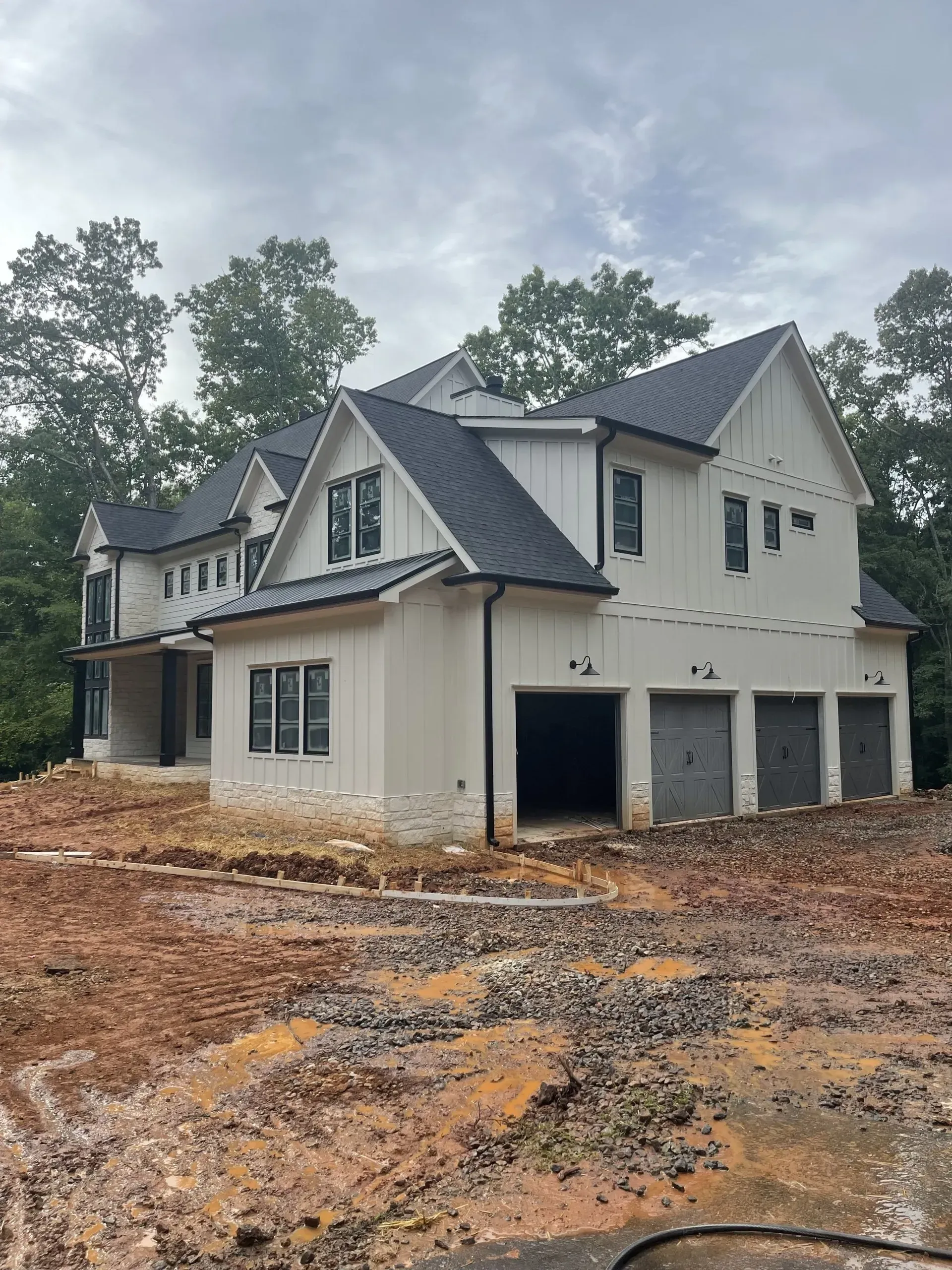 New two-story house under construction with white siding, black roof, and three-car garage.