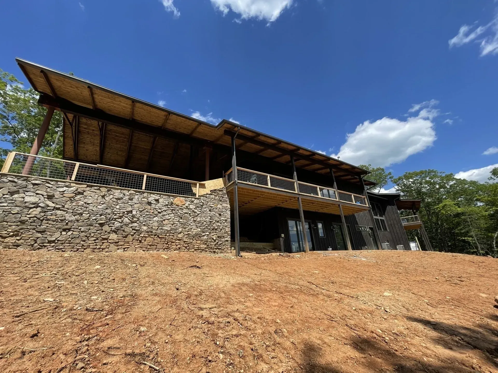 Two-story wooden building with stone base, open-air deck, and thatched roof under a blue sky.