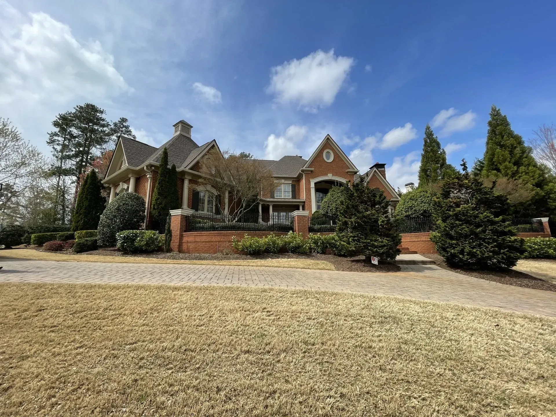 Large brick house with manicured landscaping under a blue sky with clouds.