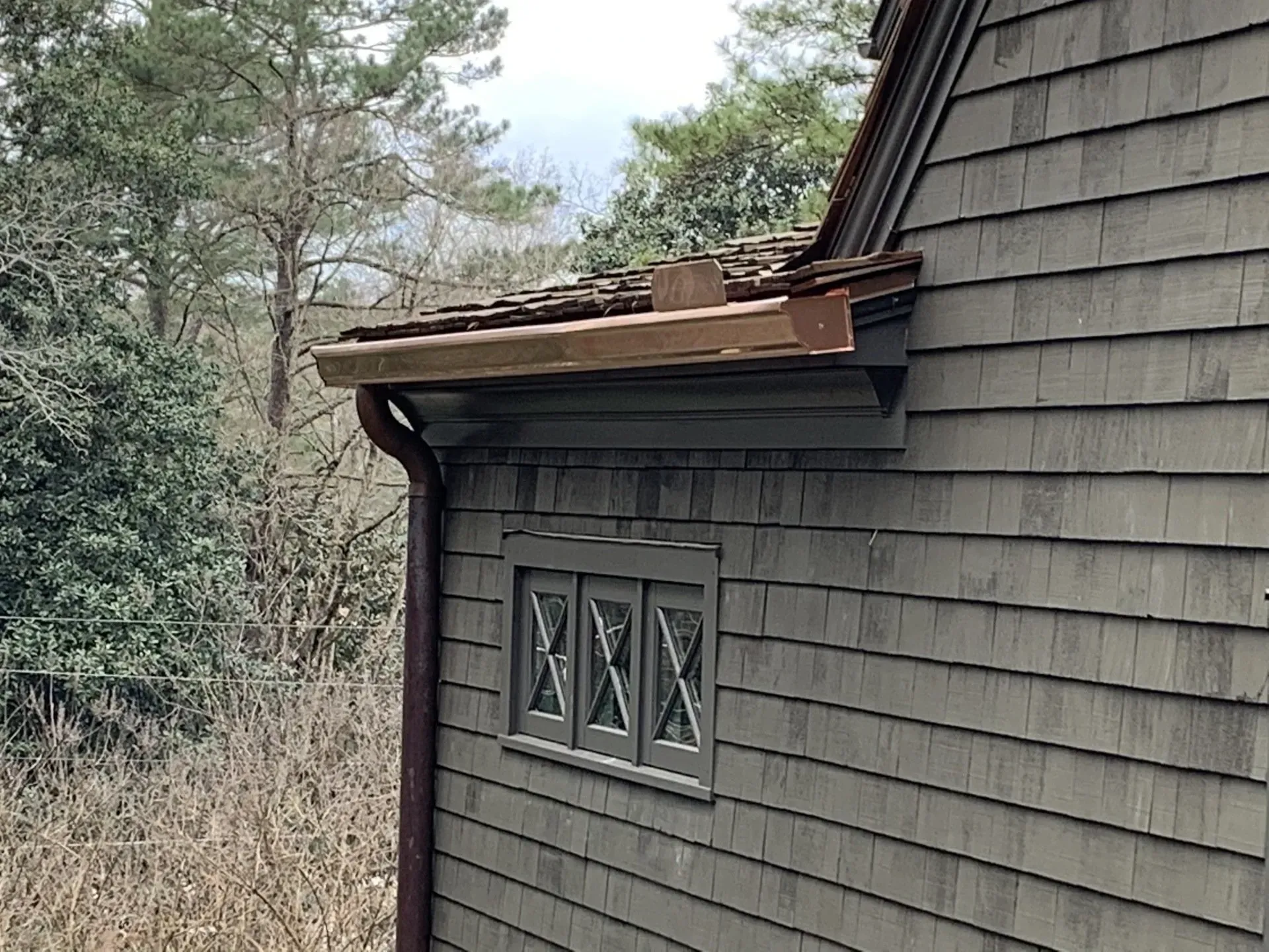 Dark gray shingled house exterior with copper gutters and a window.