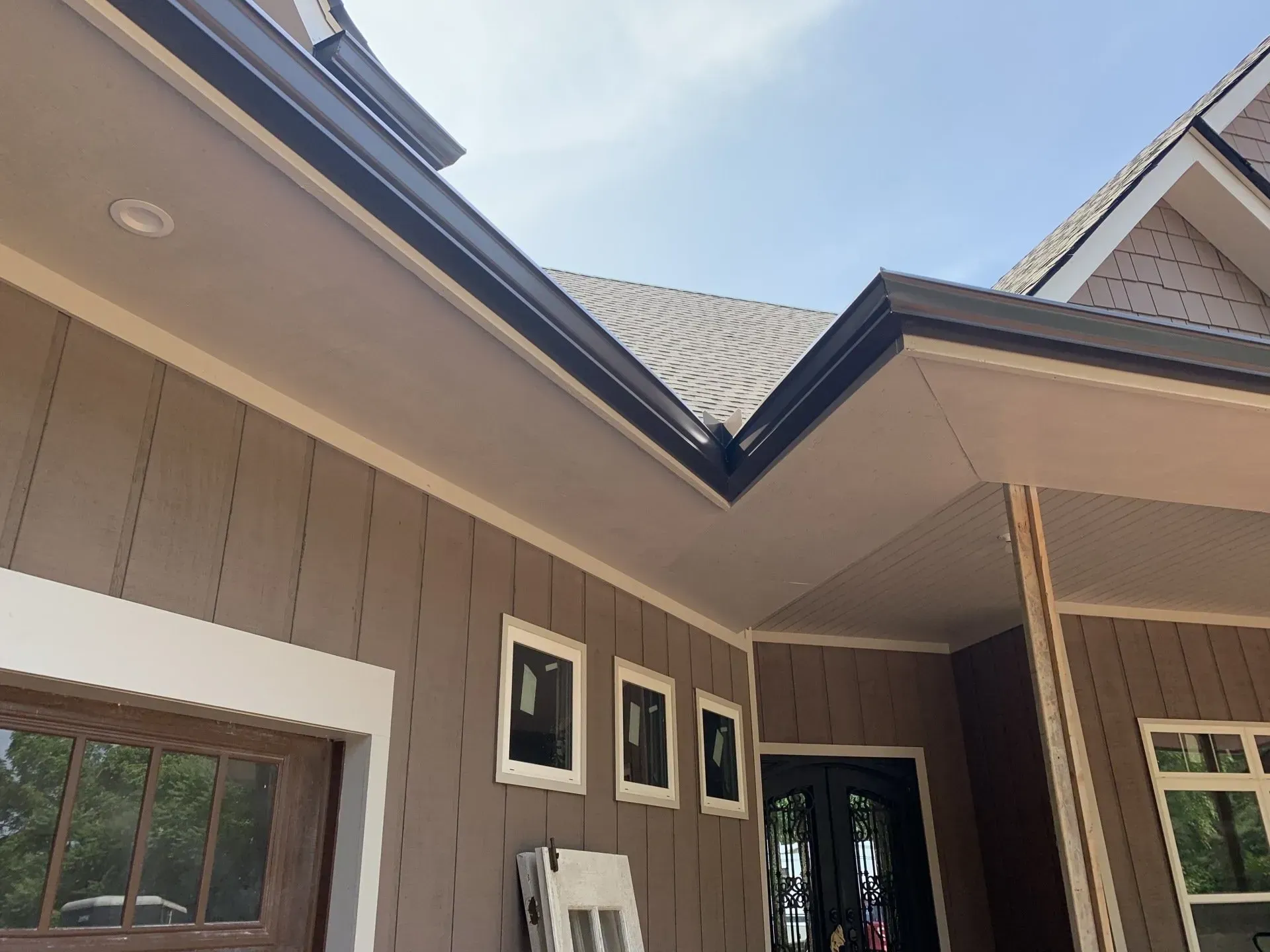 Brown siding and black gutters on a house with white trim, against a partly cloudy sky.