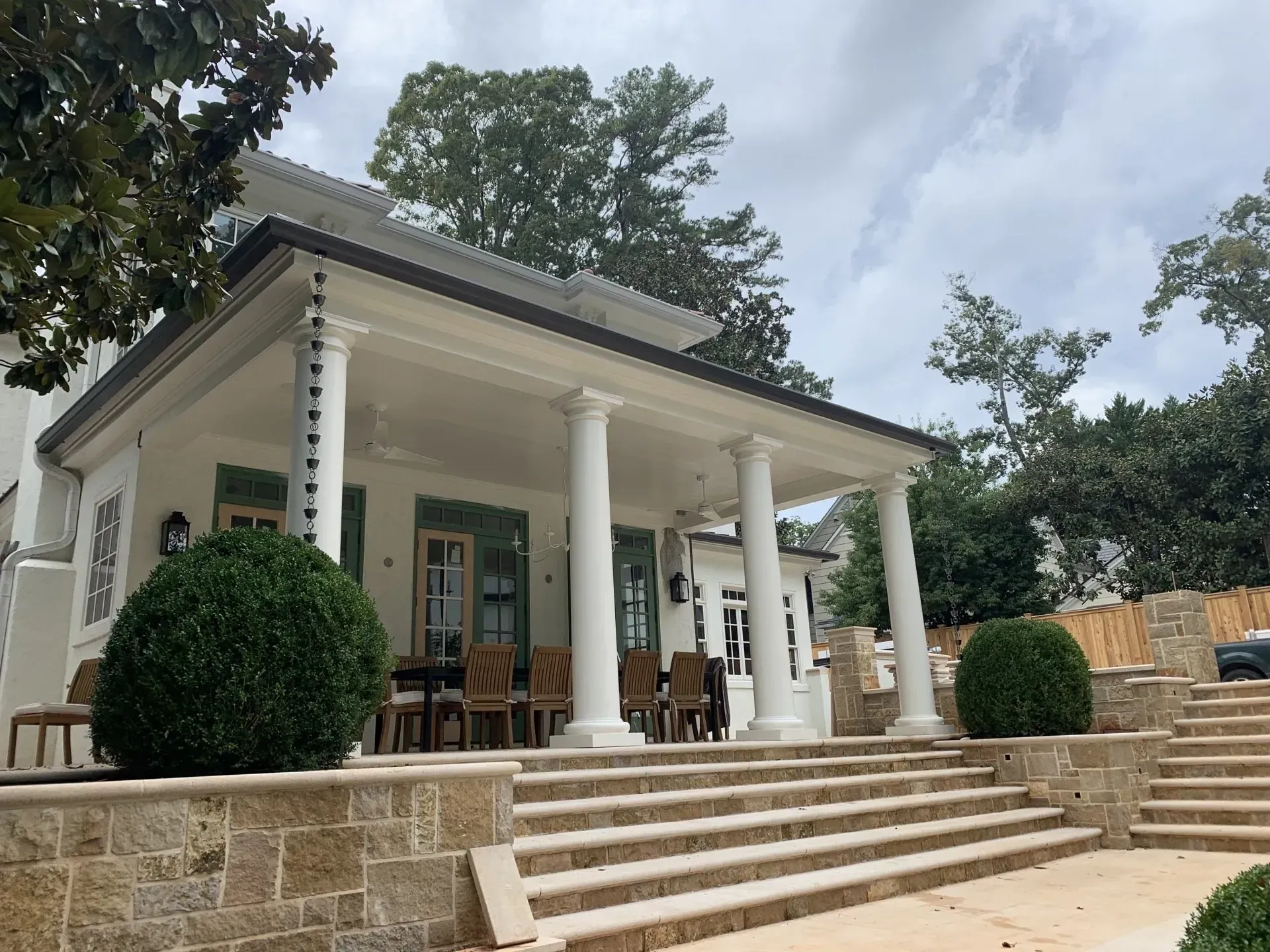 White house with columns, a covered porch, stone steps, and green shutters.