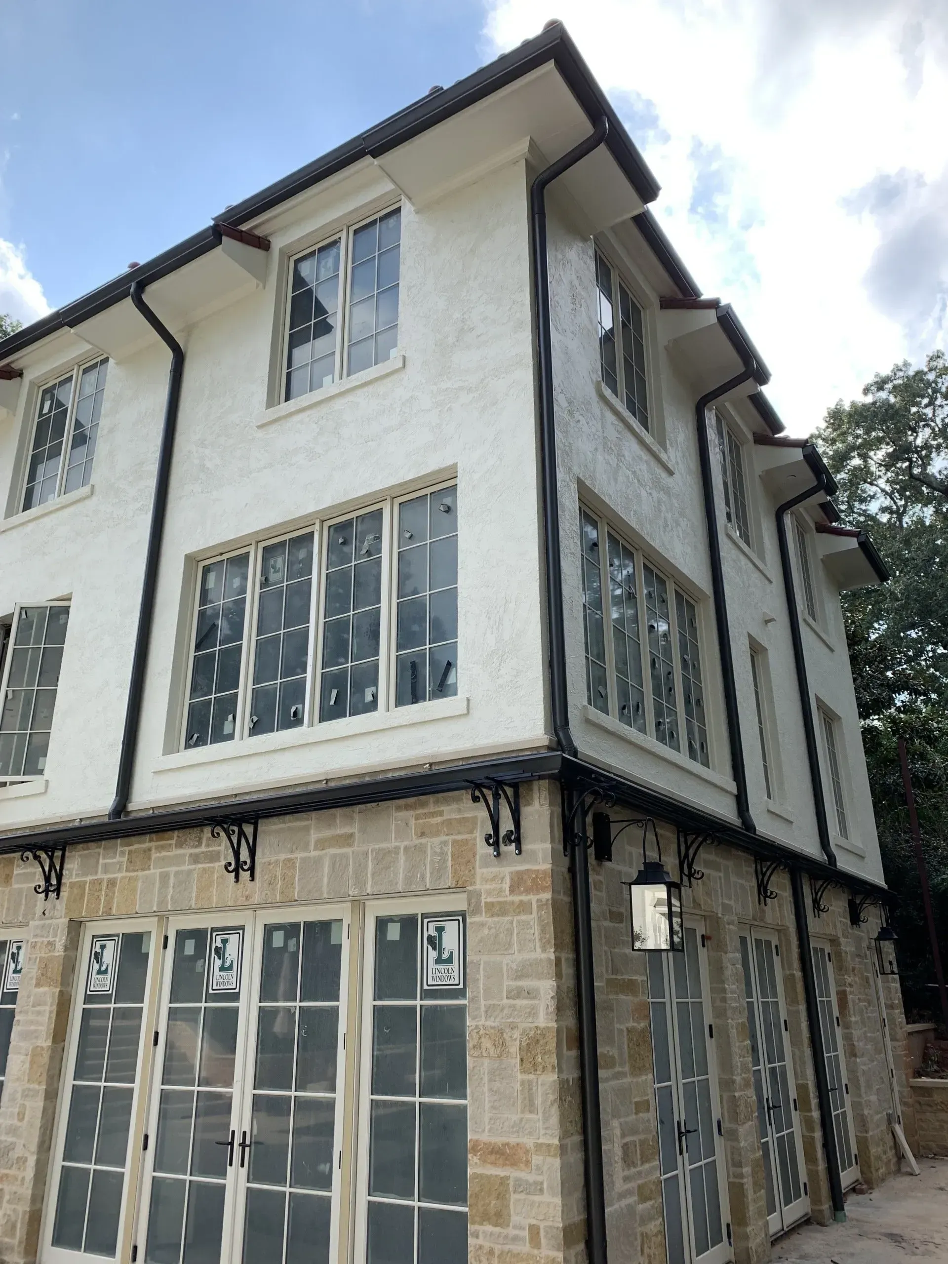 Two-story building with white stucco upper level, stone lower level, and black gutters.