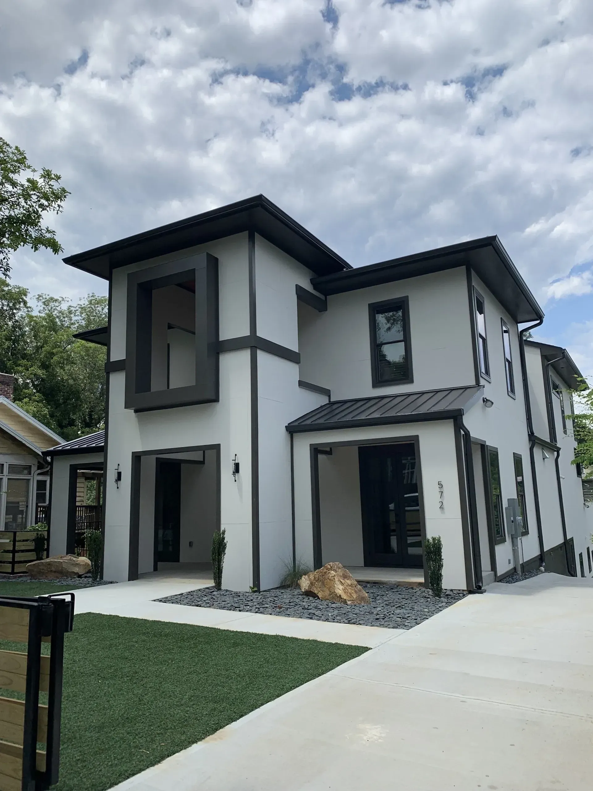 Modern two-story house with white stucco walls, black trim, and a concrete driveway.