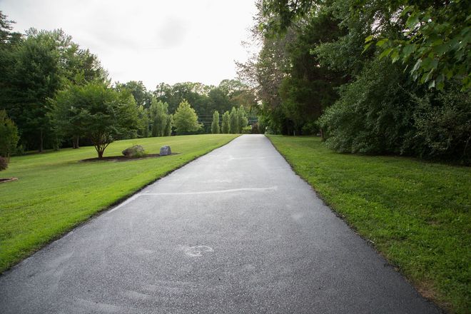 Asphalt driveway flanked by green lawns and trees, leading to a lighter horizon.