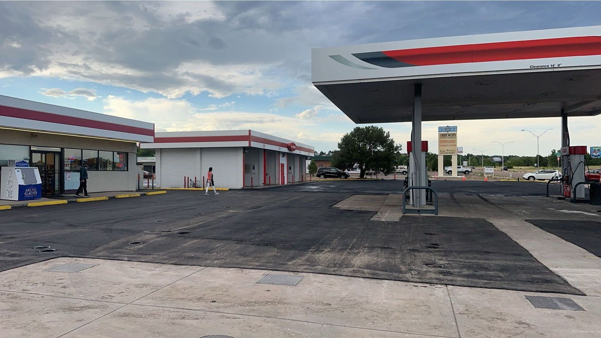 Gas station exterior with multiple pumps and canopy, asphalt and gravel ground, cloudy sky.