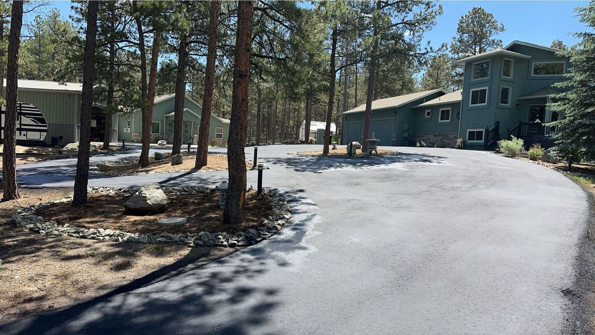Asphalt driveway leading to a multi-story teal-colored house surrounded by trees.