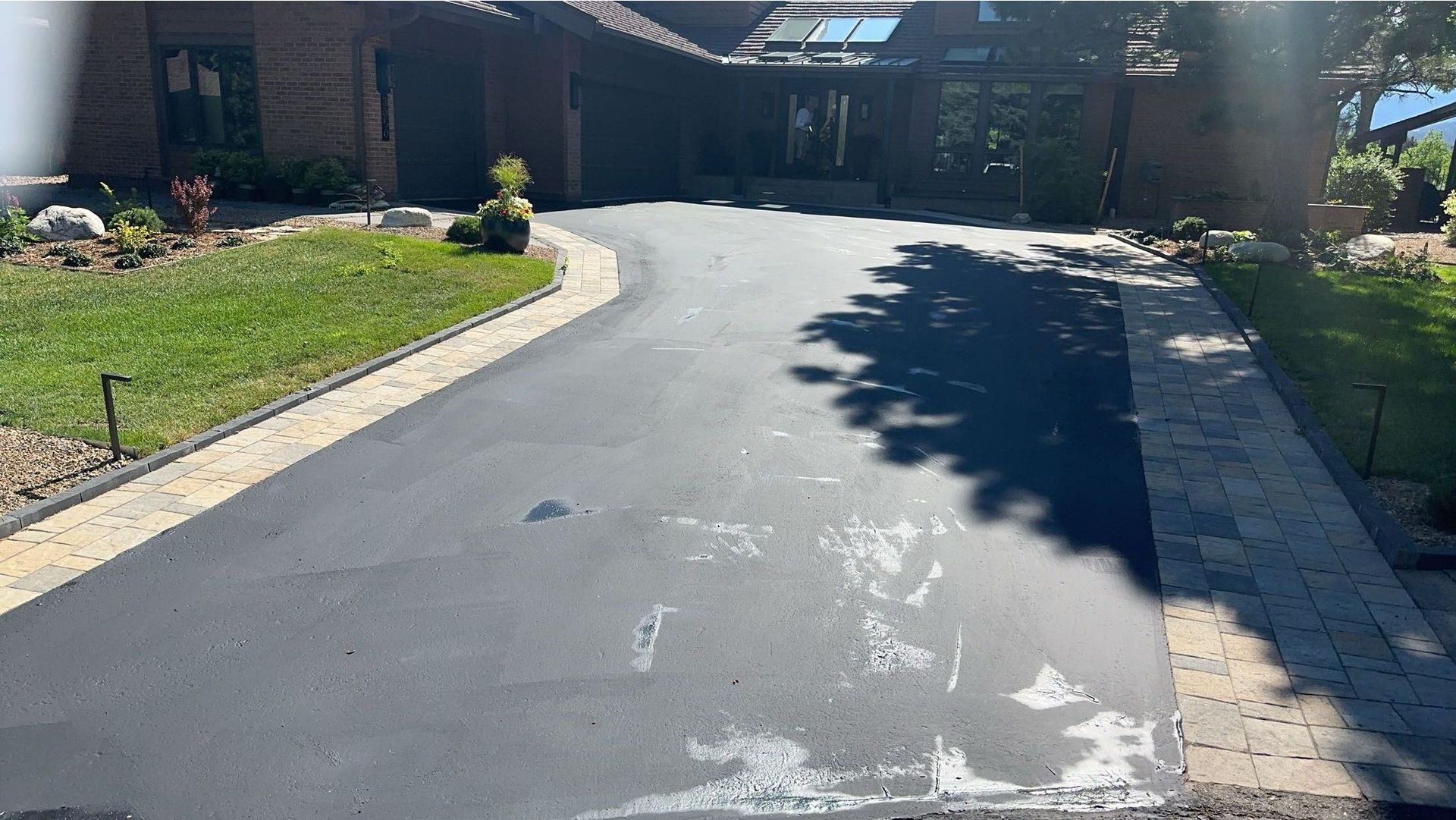 Asphalt driveway leading to a house with a dark facade; green lawn on either side.