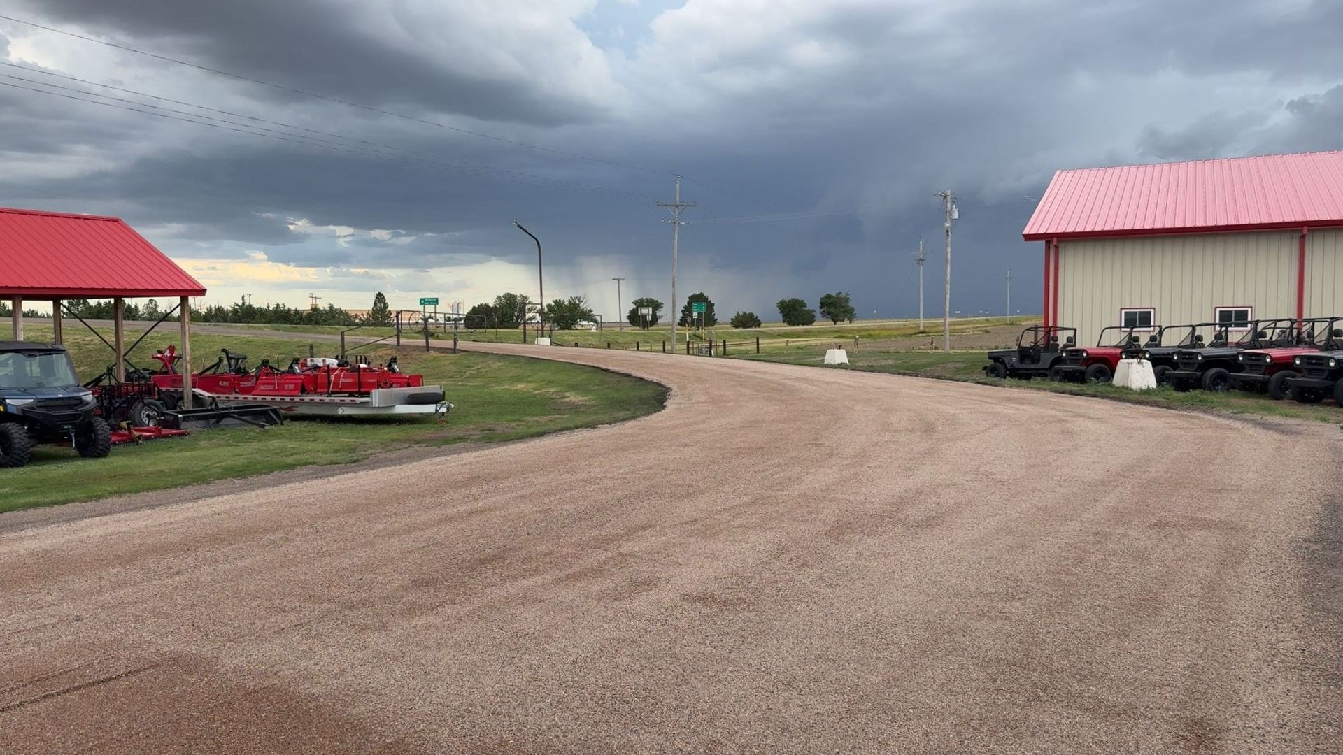 Gravel driveway curves between red-roofed buildings; storm clouds loom overhead.
