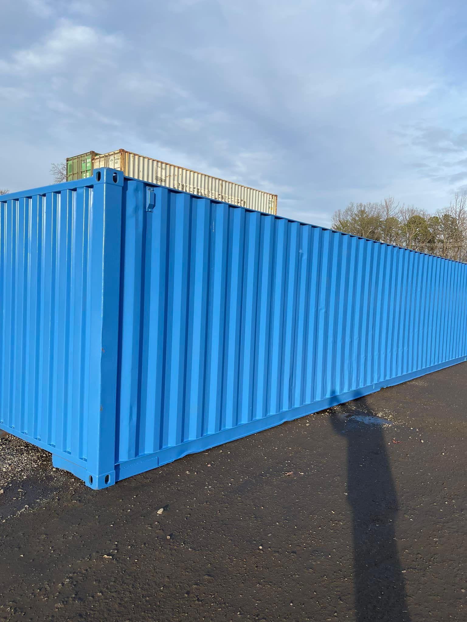 A bright blue shipping container sits outdoors on a gravel lot under a clear sky.