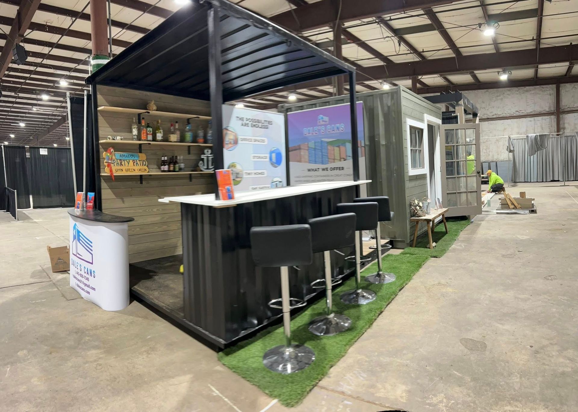 Outdoor bar kiosk with black counter and stools inside a warehouse-style space