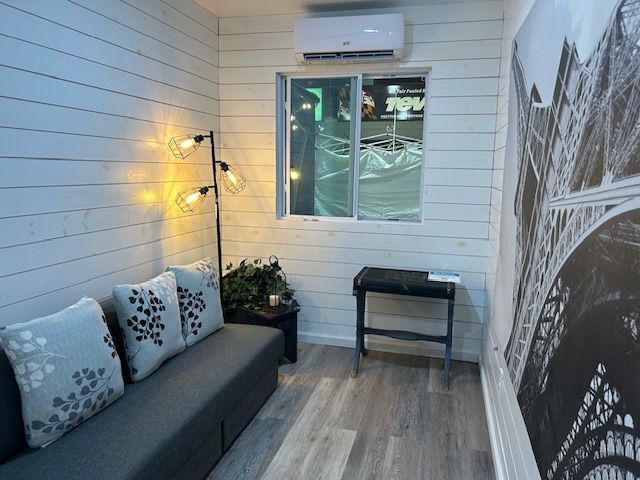 A cozy room with white shiplap walls, a grey sofa with patterned pillows, a floor lamp, a window, and wall art.