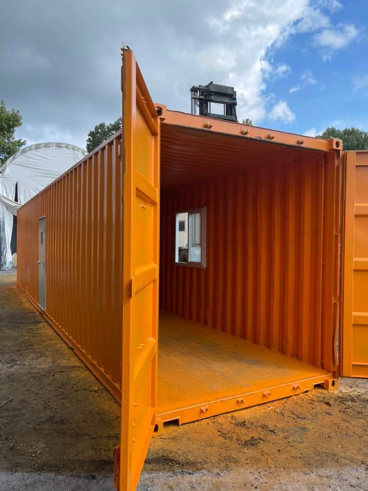 A bright orange shipping container with an open end, showing an interior window and a side entry door.