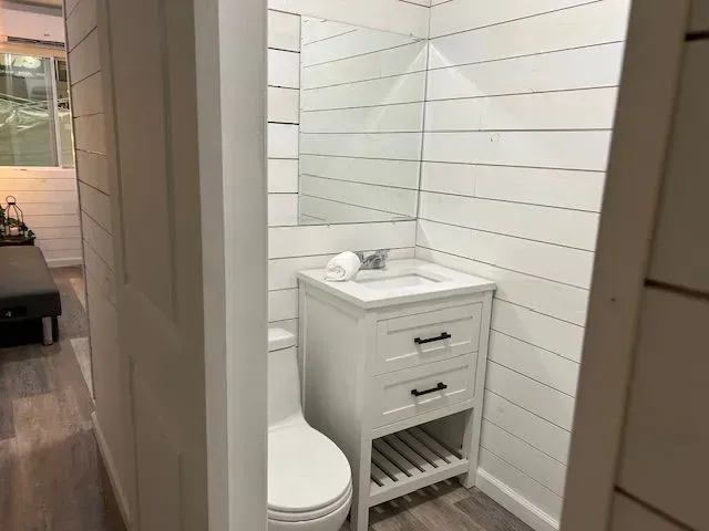 A bathroom with white shiplap walls, a white vanity with drawers and an open shelf, and a white toilet.