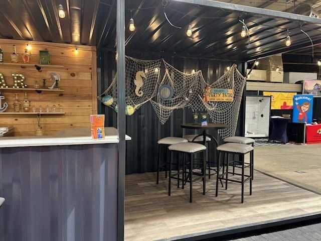 An orange shipping container converted into a food stall with a large open service window, situated in an indoor space.