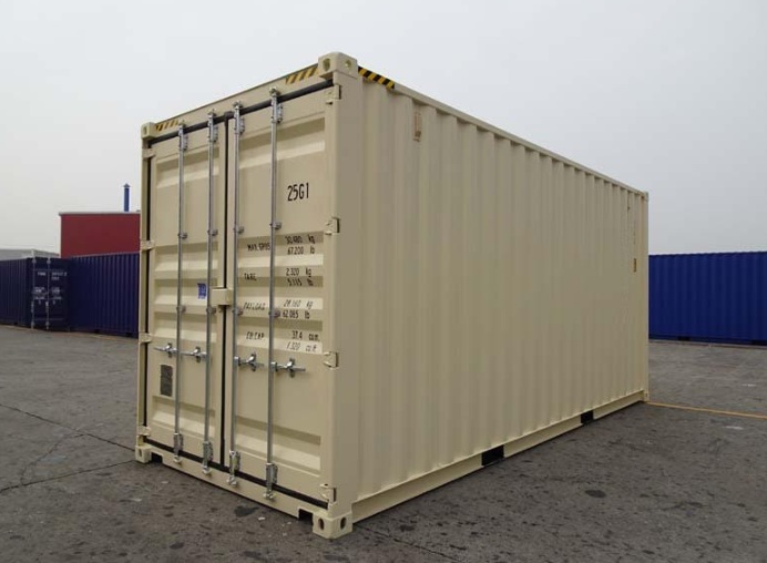 A beige shipping container stands on a grey paved lot surrounded by other containers under an overcast sky.