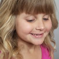 A little girl with blonde hair and a pink shirt is smiling.