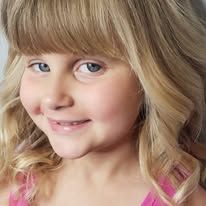 A little girl with blonde hair and blue eyes is smiling for the camera.