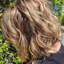 A woman with long wavy brown hair is wearing a black shirt.