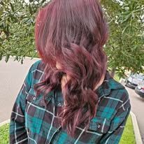 A woman with purple hair is wearing a plaid shirt and covering her face.