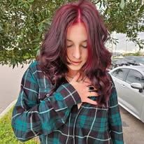 A woman with red hair is wearing a plaid shirt and standing in front of a car.
