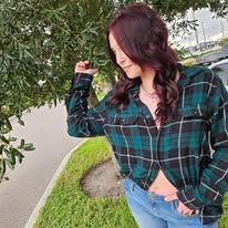 A woman wearing a plaid shirt and jeans is standing next to a tree.