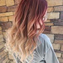 A woman with long red hair is standing in front of a brick wall.