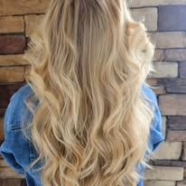 A woman with long blonde hair is standing in front of a brick wall.