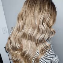 A woman with long blonde wavy hair is wearing a plaid shirt.