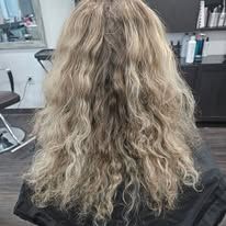 A woman with long blonde curly hair is sitting in a chair in a salon.