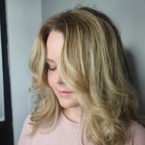 A woman with long blonde hair is wearing a pink shirt.