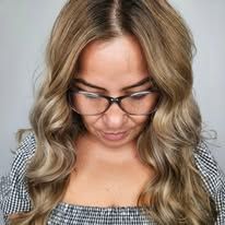 A woman wearing glasses and a plaid shirt is looking down at her hair.