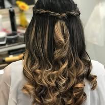 A woman with long curly hair is wearing a braided half up half down hairstyle.