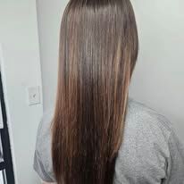 A woman with long straight brown hair is wearing a grey shirt.