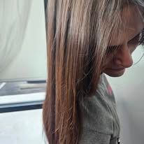 A woman with long brown hair is looking down at her hair.