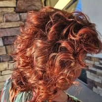 A woman with red curly hair is standing in front of a brick wall.