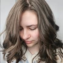 A woman with long brown hair is wearing a sweater and looking down.
