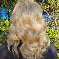 A woman with long blonde hair is standing in front of a tree.