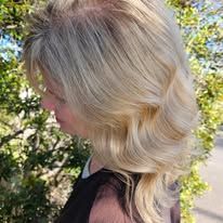 A woman with blonde hair is standing in front of a tree.