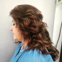 A woman with long brown hair is wearing a blue shirt and a necklace.