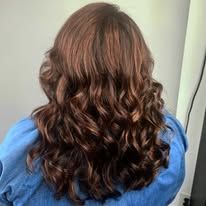 A woman with long brown curly hair is wearing a blue shirt.