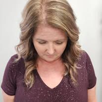 A woman in a purple shirt is looking down at her hair.